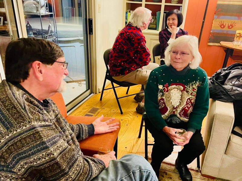 Four people sit in a cozy room having a conversation. One person is wearing a festive sweater with a Santa design.