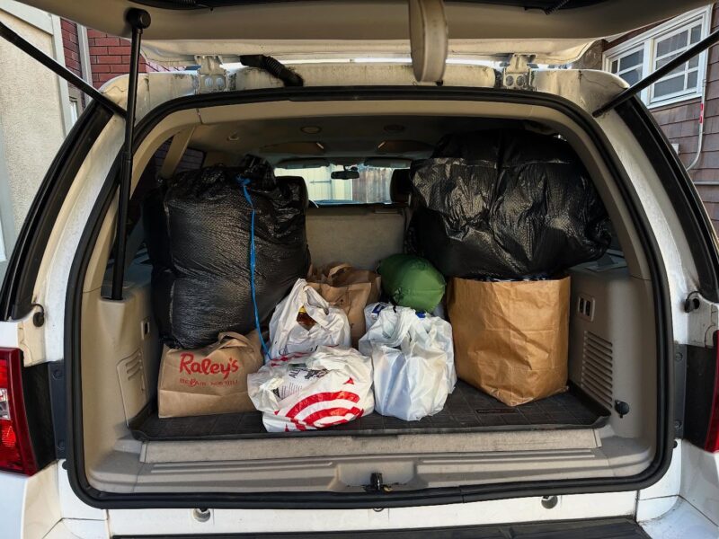 An SUV trunk filled with various bags, including Raley’s and Target. Large black trash bags are stacked inside. No people visible.